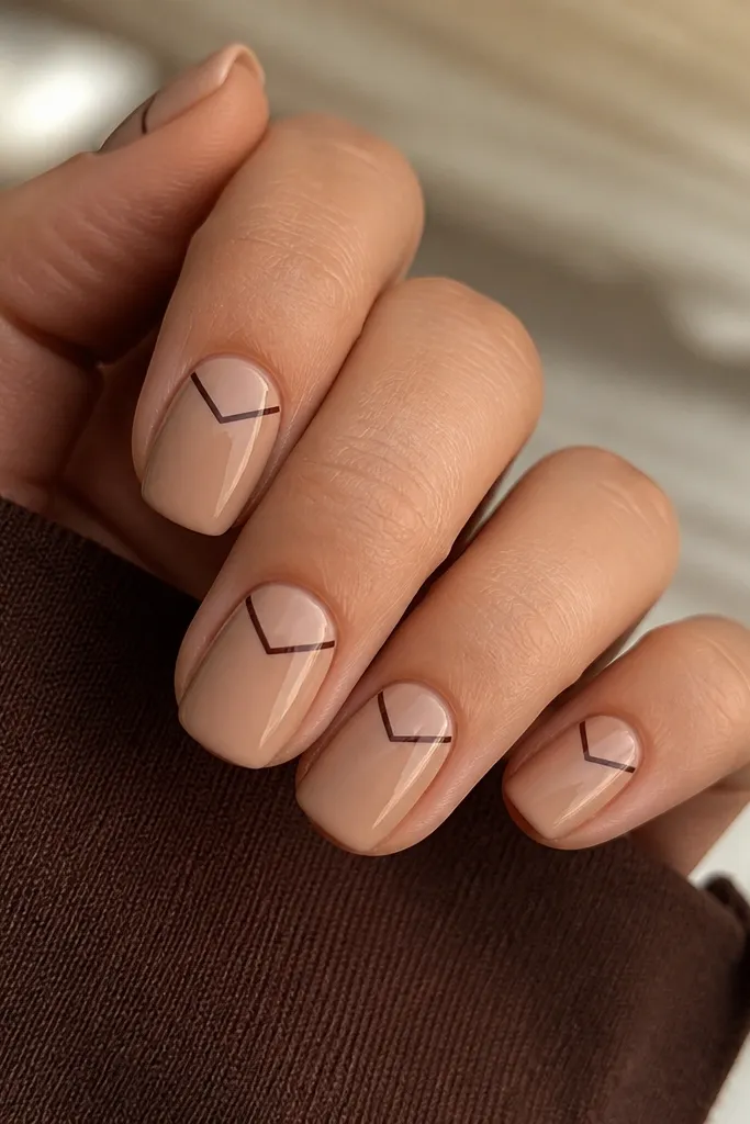 Short squoval nails in warm nude with a single thin chocolate-brown chevron placed near the top third, pointing down toward the center; glossy.