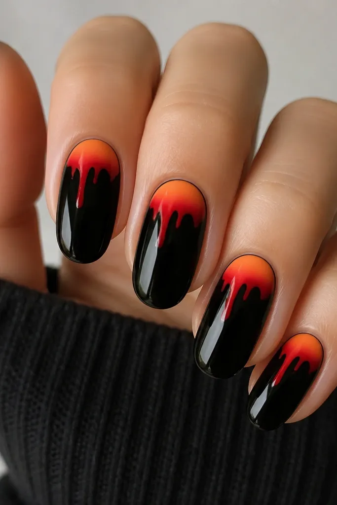 Black base nails with a small gradient patch in the center top area. Over the gradient, there are two tiny red-orange drips that hang toward the middle of the nail. Glossy finish with sharp drip edges.