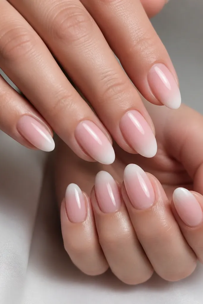 Medium-short almond nails. The base is soft pink, and the tip fades from blush to white from the smile line to the edge. No hard stripe - it's a smooth ombre gradient with a glossy finish.
