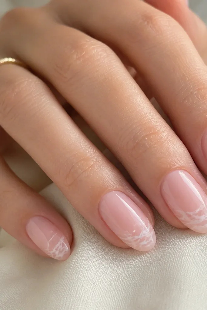 Soft pink nails with marble-style veining concentrated near the tips; the veining is sheer white and looks airy, not opaque; glossy finish.