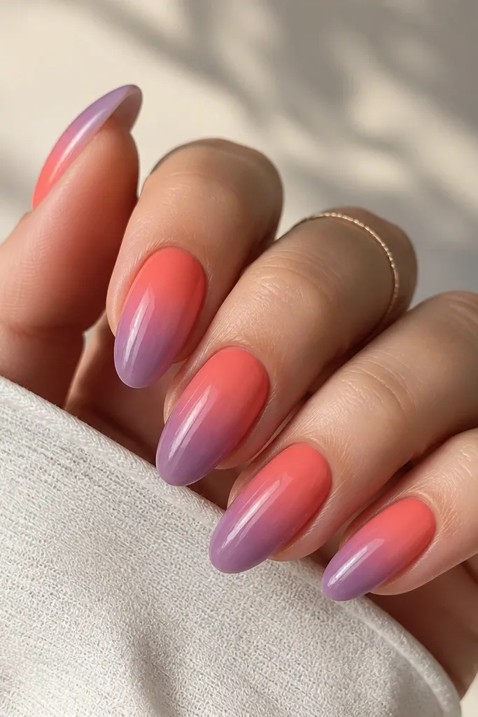 A full set of medium almond nails with a smooth gradient: coral orange near the cuticle fading into dusty violet at the tip, all under a super glossy clear coat. The gradient is even from sidewall to sidewall with no harsh band.