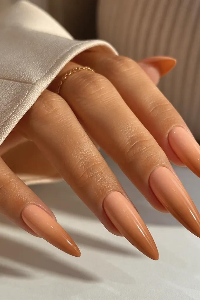 Stiletto nails with peach ombre that fades into warm caramel-brown near the tip. The transition is smooth, and the topcoat is glossy with a soft reflective sheen.