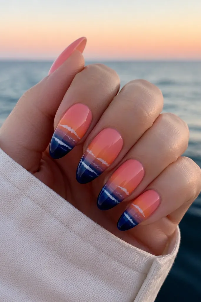 Almond nails with a sunset gradient sky above a deep navy wave line. The wave has 2-3 white highlights like foam, and the navy fades upward into the pink/orange sky.