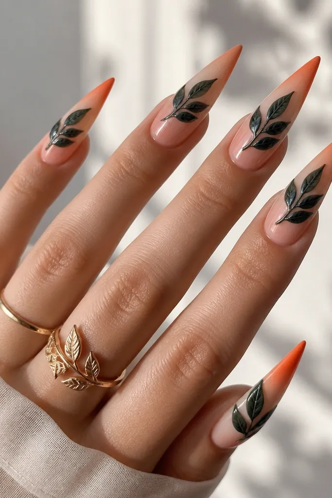 Long stiletto nails. French tips are a glossy gradient from sheer peach to orange-red. Leaves are painted in deep green, then clear gel veins are added on top so they look glassy and raised slightly. The effect is shiny and dimensional.