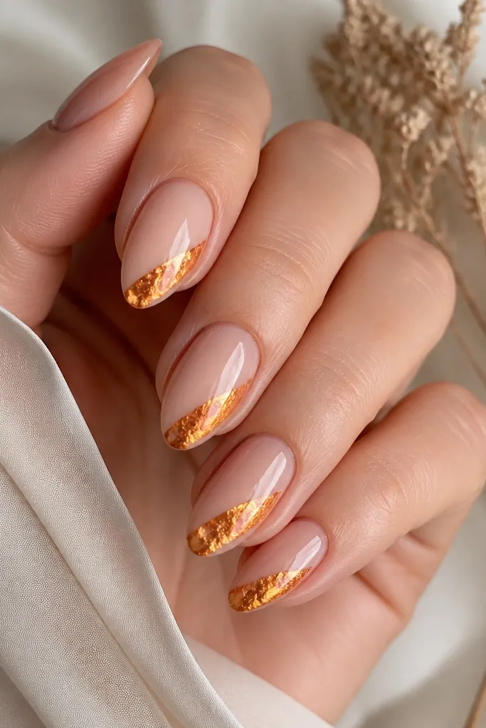 Each nail has a nude-pink base with a single diagonal strip of orange-gold foil running from mid-nail to the tip corner; glossy top coat over the foil.