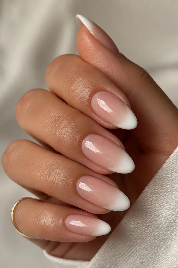 Almond nails with warm nude base; creamy white French tips have a blended, airbrushed edge; glossy finish; no other art.