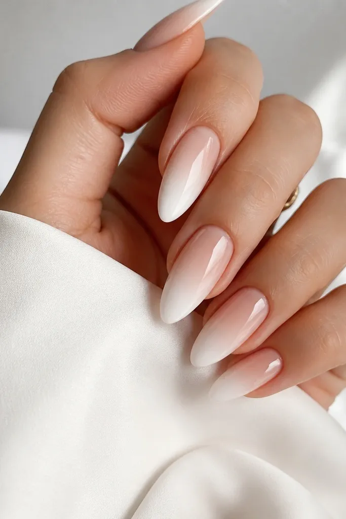 Almond nails with a white fade that starts at the tips and blends into nude near mid-nail; the gradient is smooth and glossy.