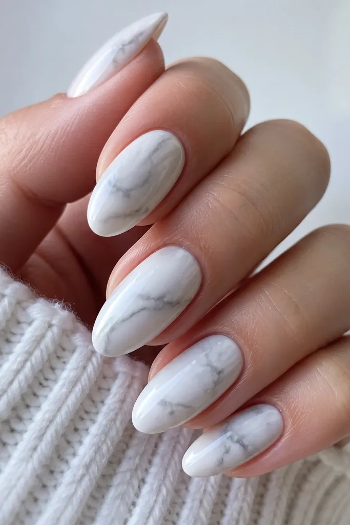 Glossy almond nails with a marble effect made of soft gray veining over a milky white base; swirls look cloudy, not drawn lines.