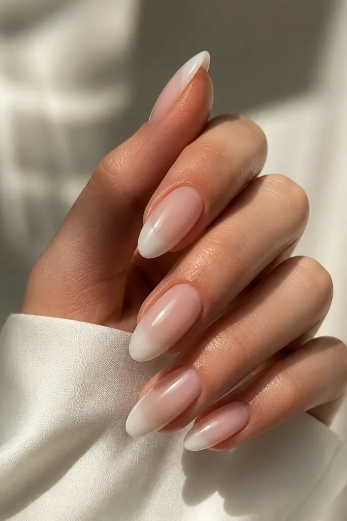 Almond nails with a sheer nude base. The French tip is white but fades from solid near the tip edge to transparent toward the center, like a soft ombre. Finish is glossy.