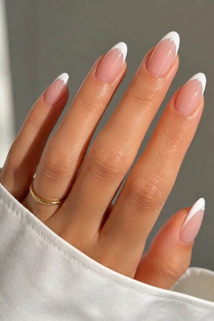 Almond nails with sheer nude base and crisp bright white French tips. At each side corner of the white tip, there's a tiny white dot, like a mini pearl. Nails are glossy.