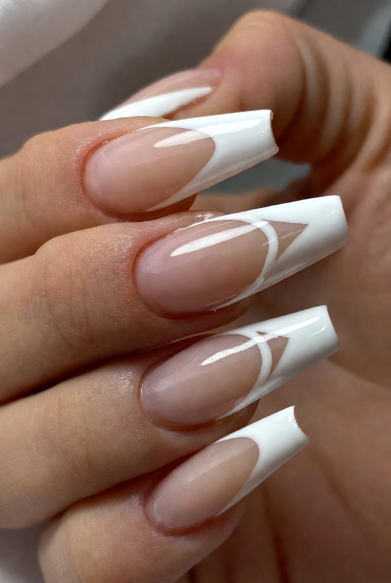 Almond nails with a sheer nude base. The French tip is white, but there's a sharp negative-space V notch cut into the center of the white, revealing nude beneath. The V is crisp and centered.
