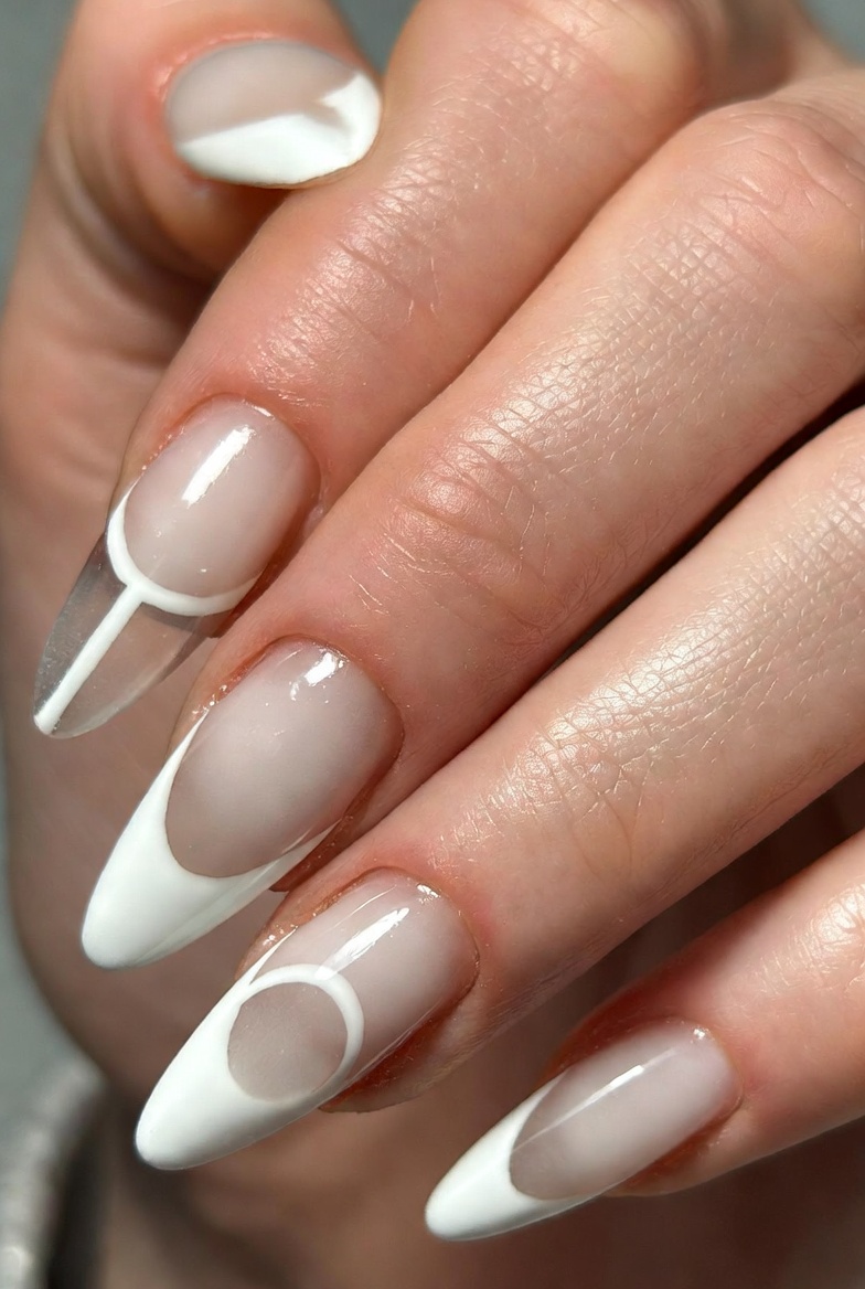 Almond nails with sheer nude base. Half-moon shapes at the cuticle are painted white, leaving the rest nude. No other decoration.