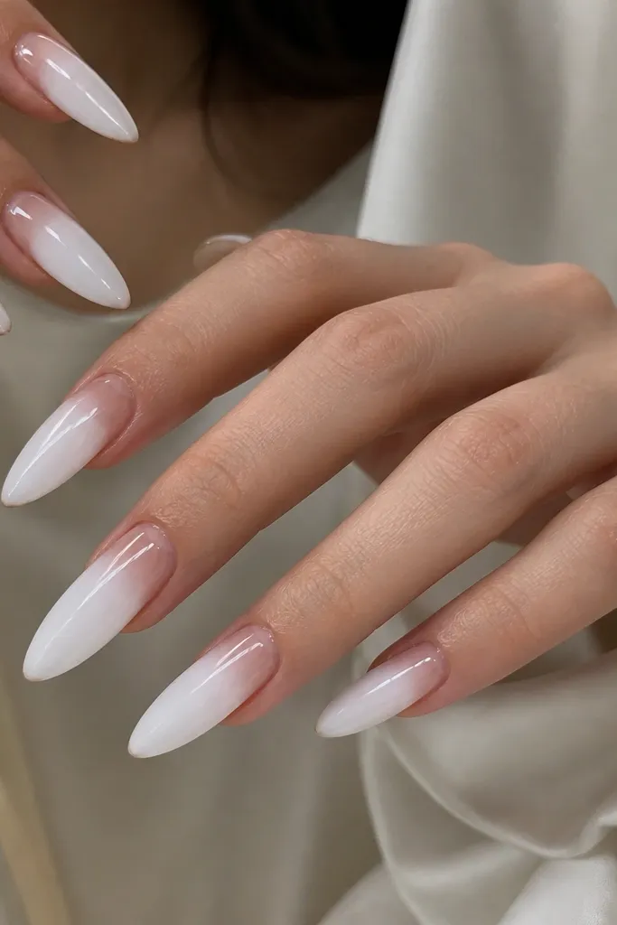 Long white almond nails with a milky glossy white base. The cuticle area is transparent and looks like clear gel glass, with a smooth curved line separating cuticle and white.