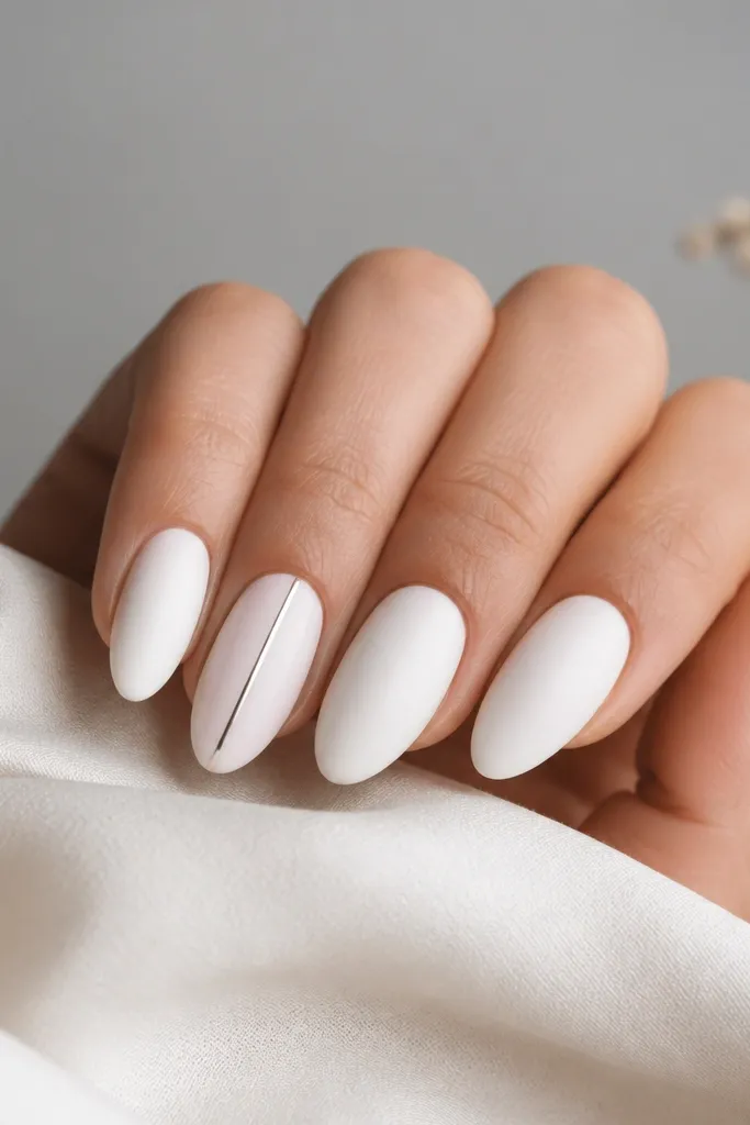 Satin-finish white almond nails. One nail has a thin metallic stripe running vertically near the side, while other nails stay plain satin white.