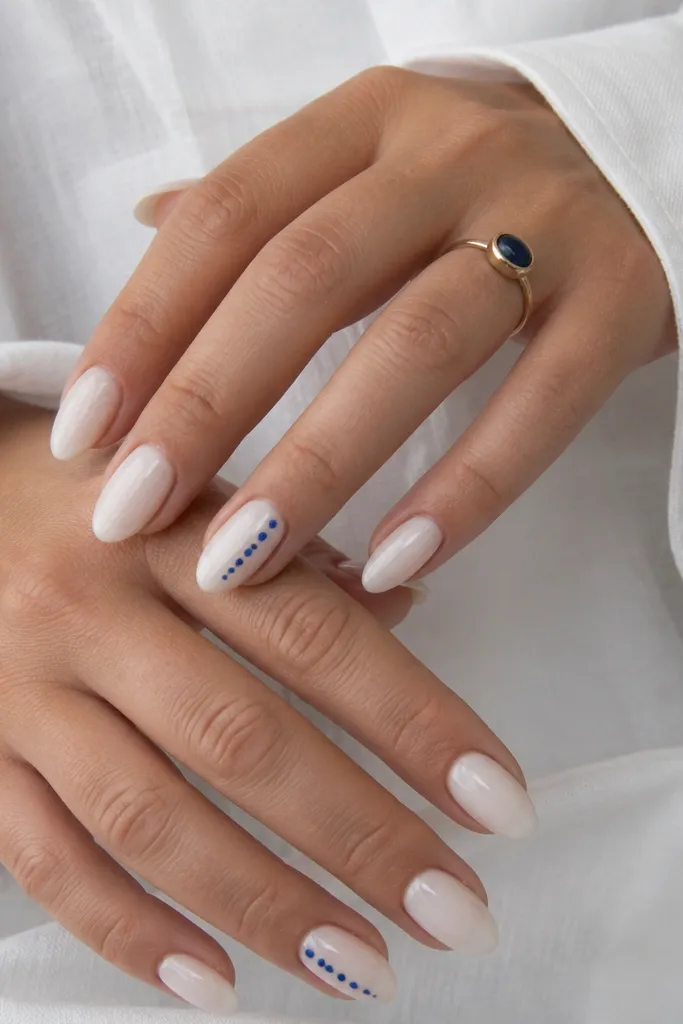Milky white almond nails with a diagonal line of tiny cobalt-blue dots on two accent nails. Dots are evenly spaced and glossy.