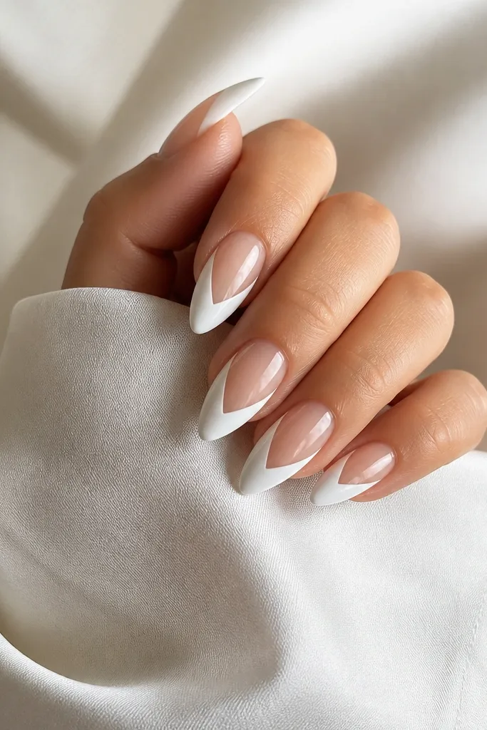 Glossy white almond nails with a V-shaped negative space near the tip. The V is clear and leaves a white border on both sides.