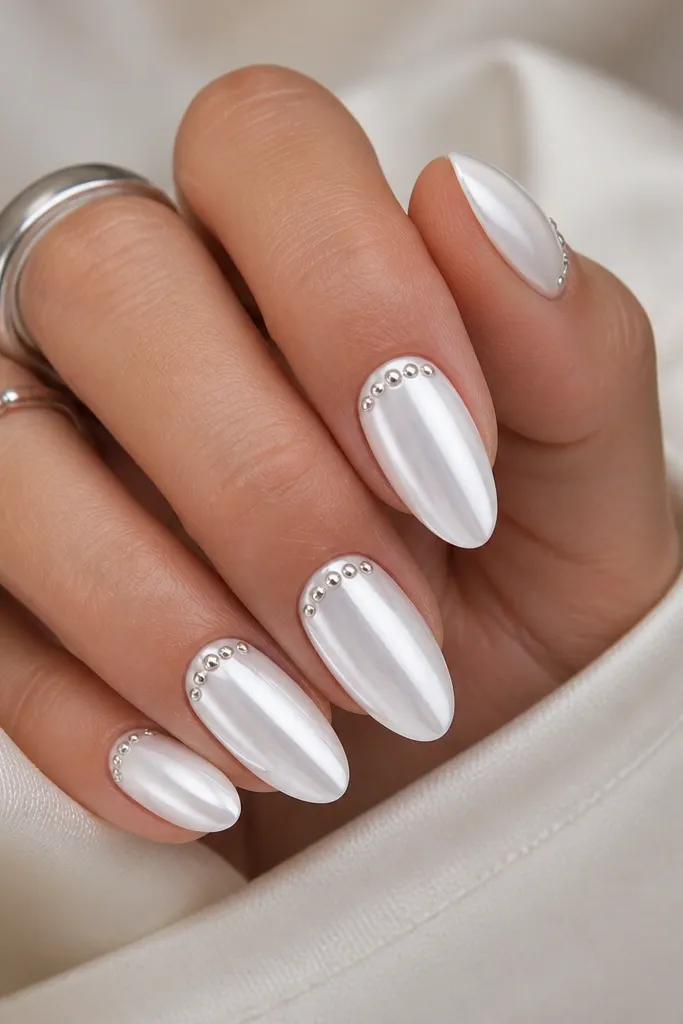 White almond chrome nails with a small curved line of silver micro dots just above the cuticle on each nail.