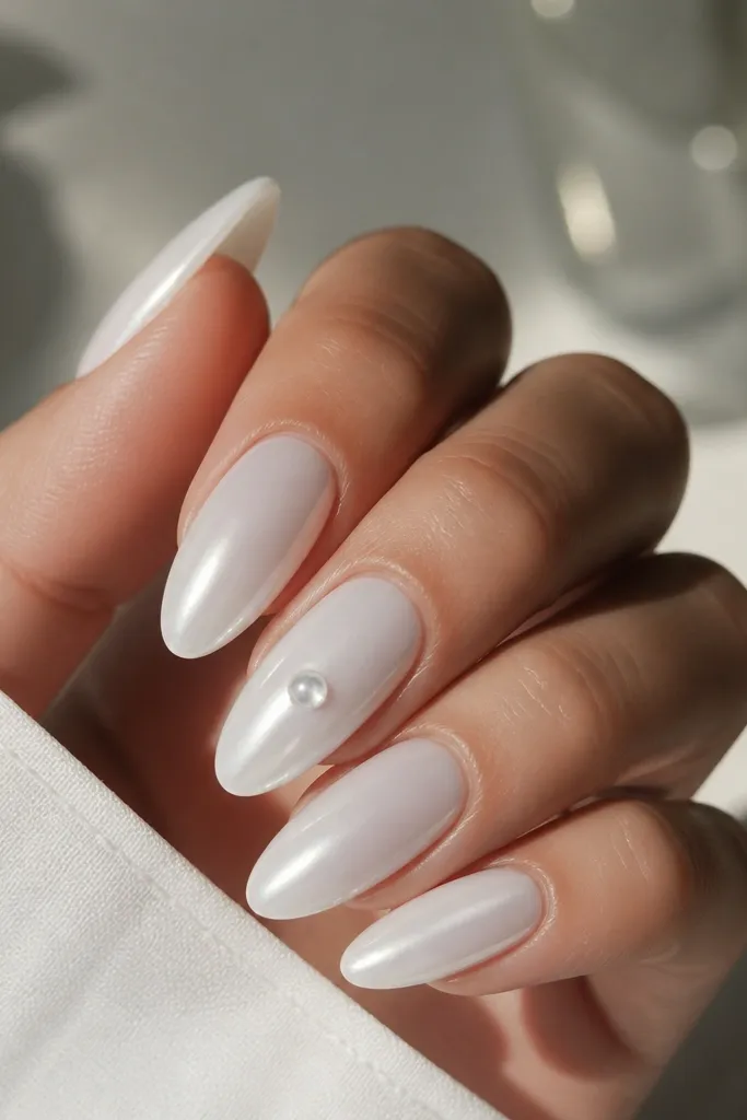 Mostly white chrome almond nails with one nail featuring a single clear glass bead near the center, glossy and reflective.