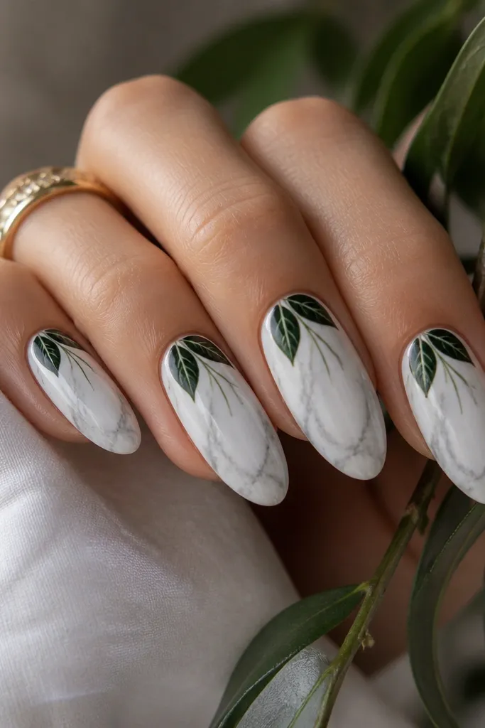 White almond nails with subtle marble veining in soft gray. Over it, deep green leaves sit near the cuticle with thin lighter-green veins running down the center.