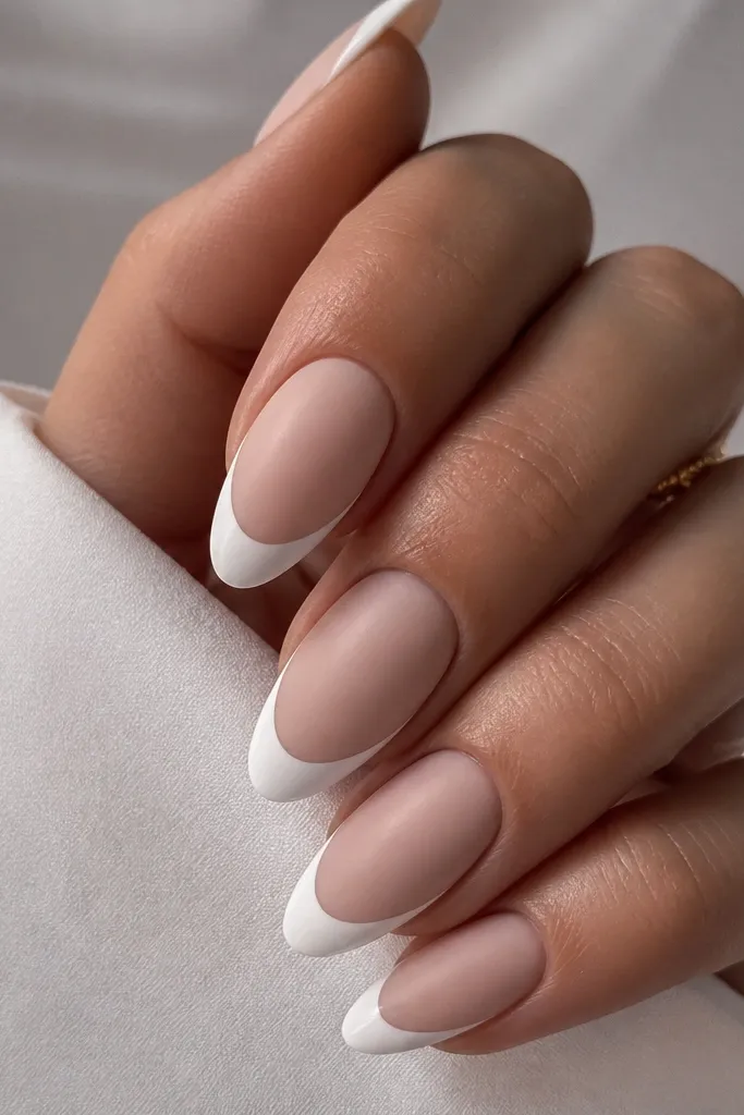 White almond nails with a matte nude base and a glossy white French tip. The contrast makes the French look sharp and dimensional.