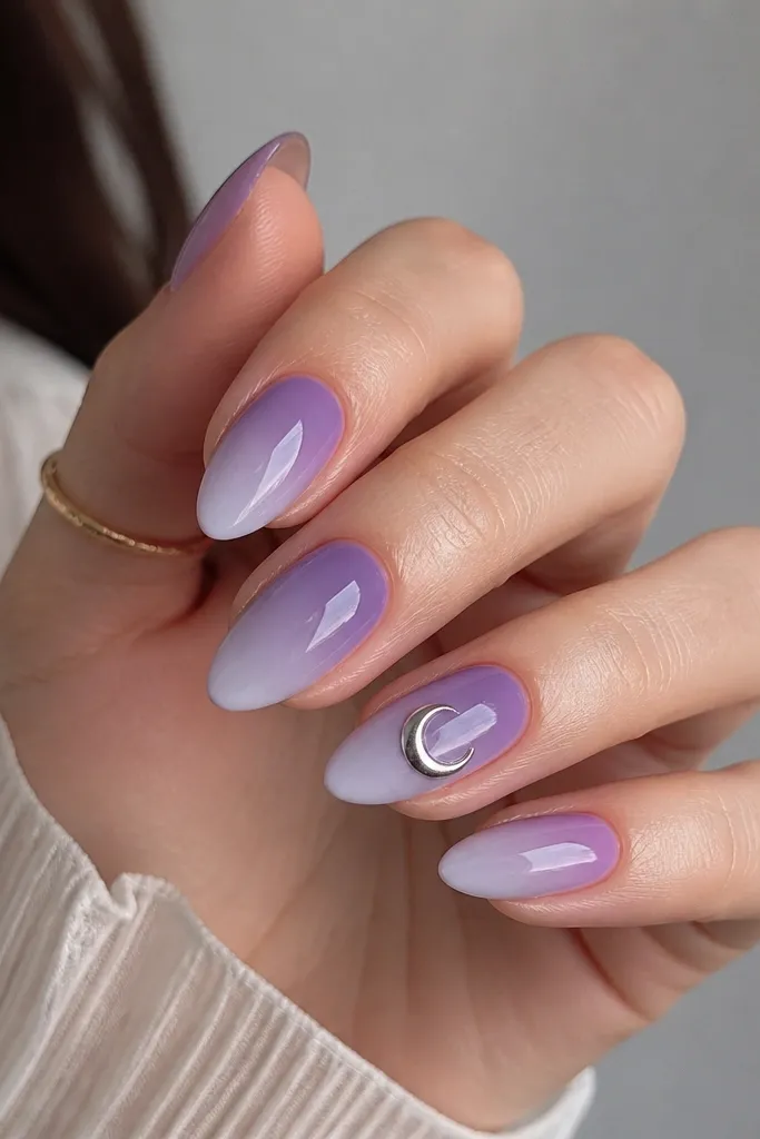 Almond nails with a soft purple-to-lavender gradient from cuticle to tip. One accent nail has a silver crescent moon shape near the center, slightly raised by gel. Glossy finish.