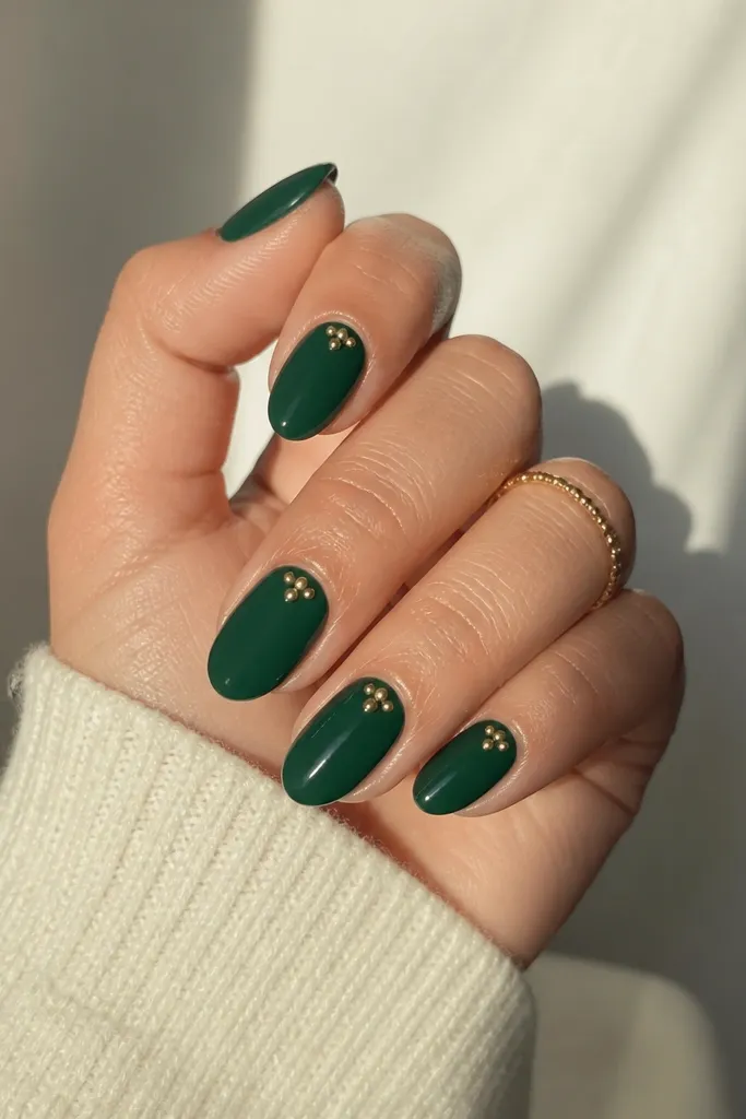 All nails are solid deep emerald. Each nail has a small cluster of three to five gold dots at the cuticle - dots vary slightly in size. The dots look like raised metal studs but are smooth.
